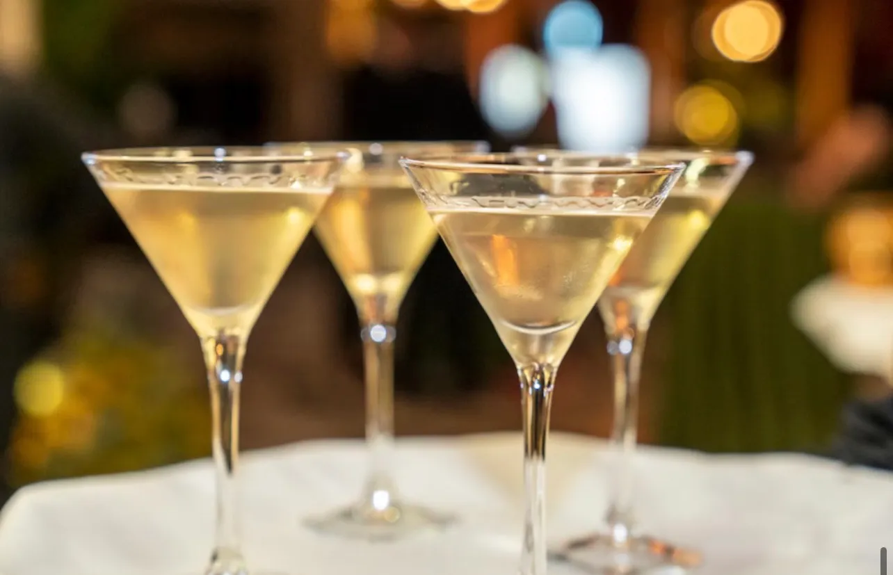 Cocktail glasses filled and waiting on a tray, the lit room out of focus behind them