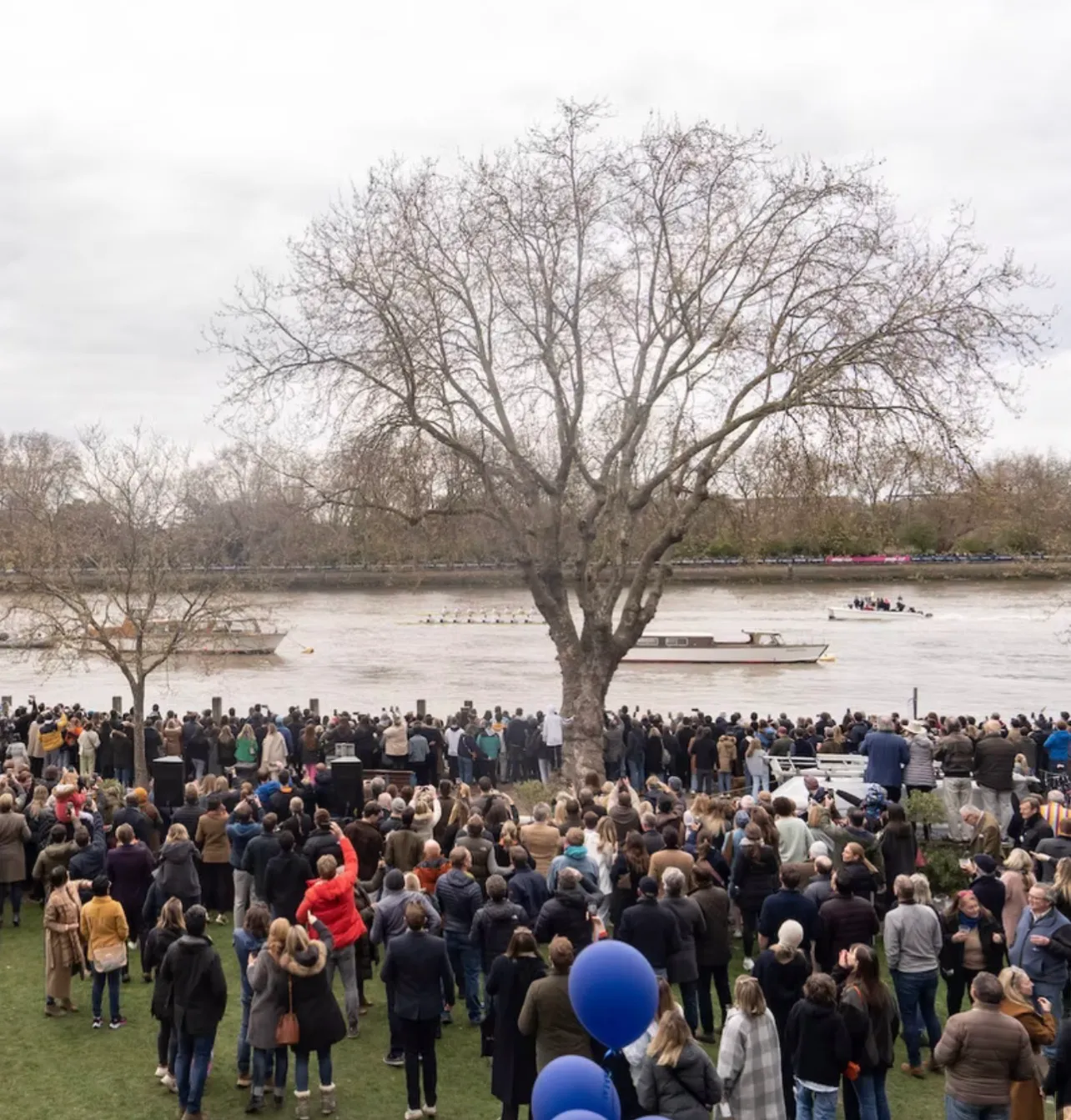 The crowd on the lawn turned to the river as a crew comes past with the launches following, balloons tied off at the front of the terrace